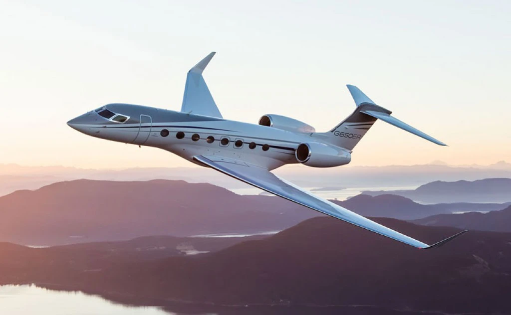 A long-range business jet in level flight above a coastline at sunset.